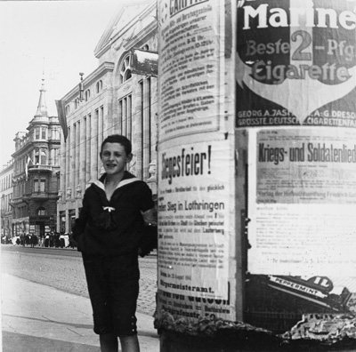 Auf den Plakatsäulen prangten 1914 Ankündigungen von Siegesfeiern. Die Aufnahme entstand in der Kaiserstraße, im Hintergrund das Warenhaus Knopf (heute Karstadt). StadtAK 8/PBS oVI 449